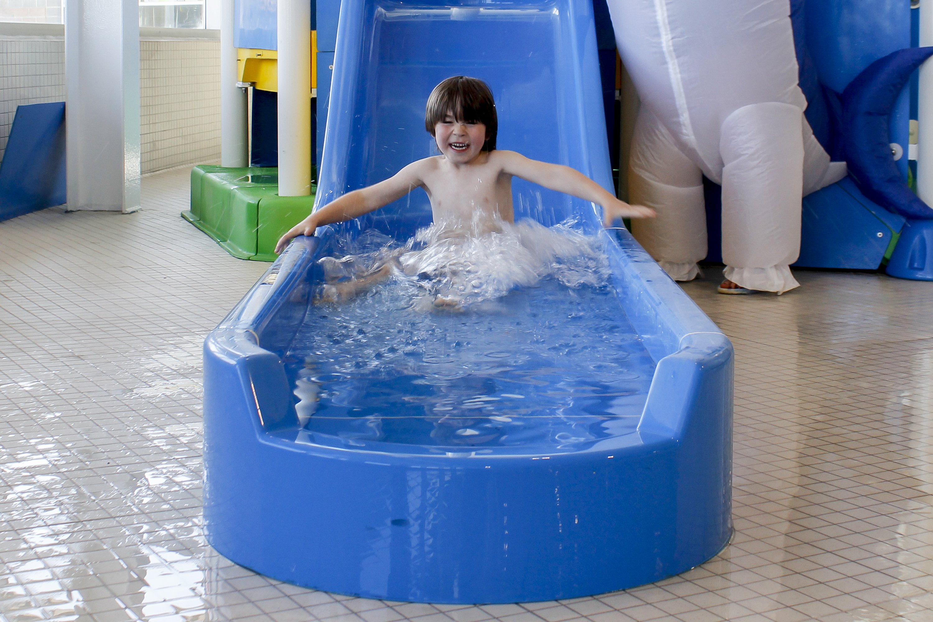 A child splashes down a blue water slide
